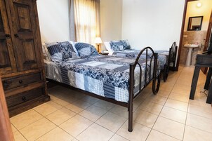 Un dormitorio con dos camas, un armario de madera, una mesita de noche con lámpara y un baño con lavamanos y espejo.