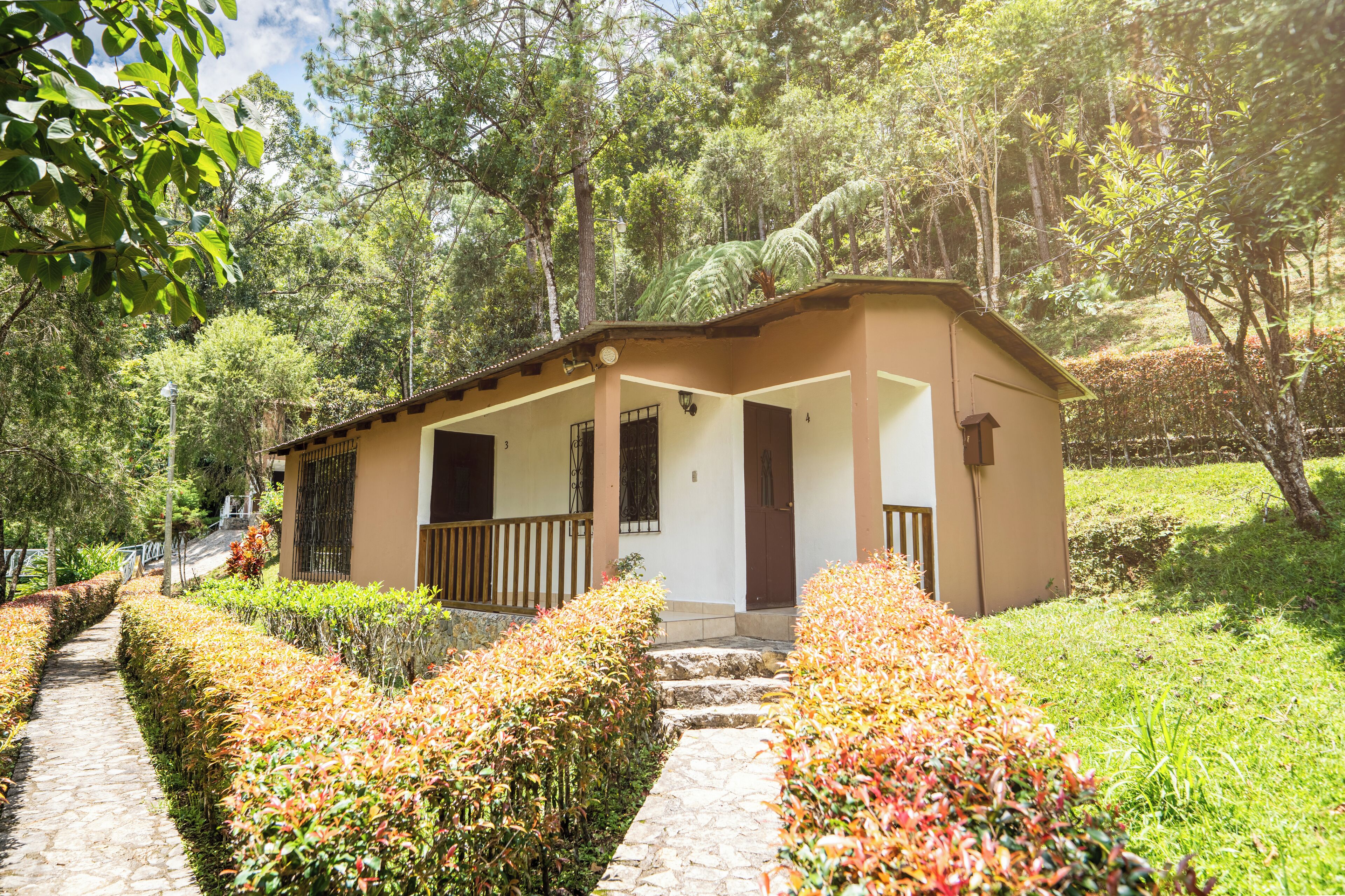 A small, single-story building with a porch, surrounded by well-maintained hedges and a stone pathway.