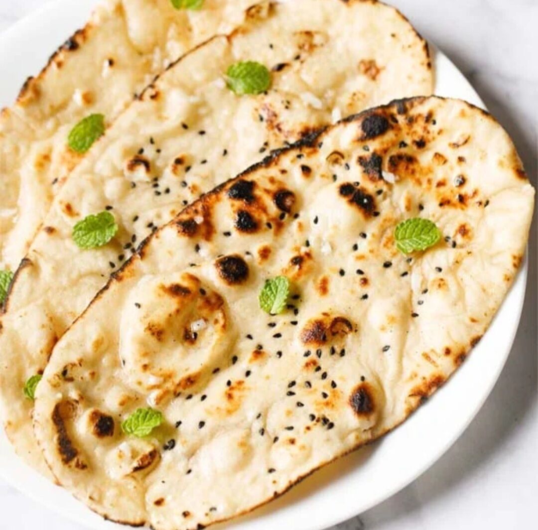 Naan bread with charred spots and mint leaves on a white plate.