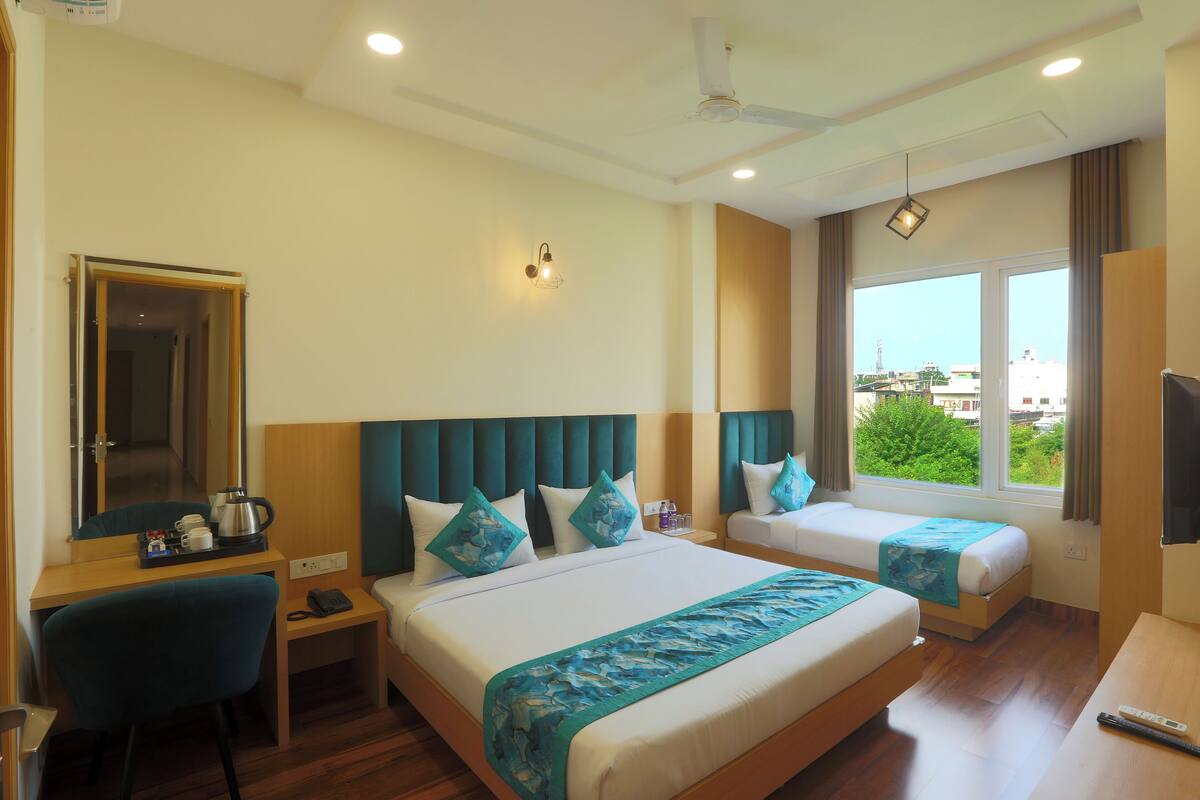 A hotel room with a bed, a desk, a chair, a nightstand, a TV, and a window with a view.