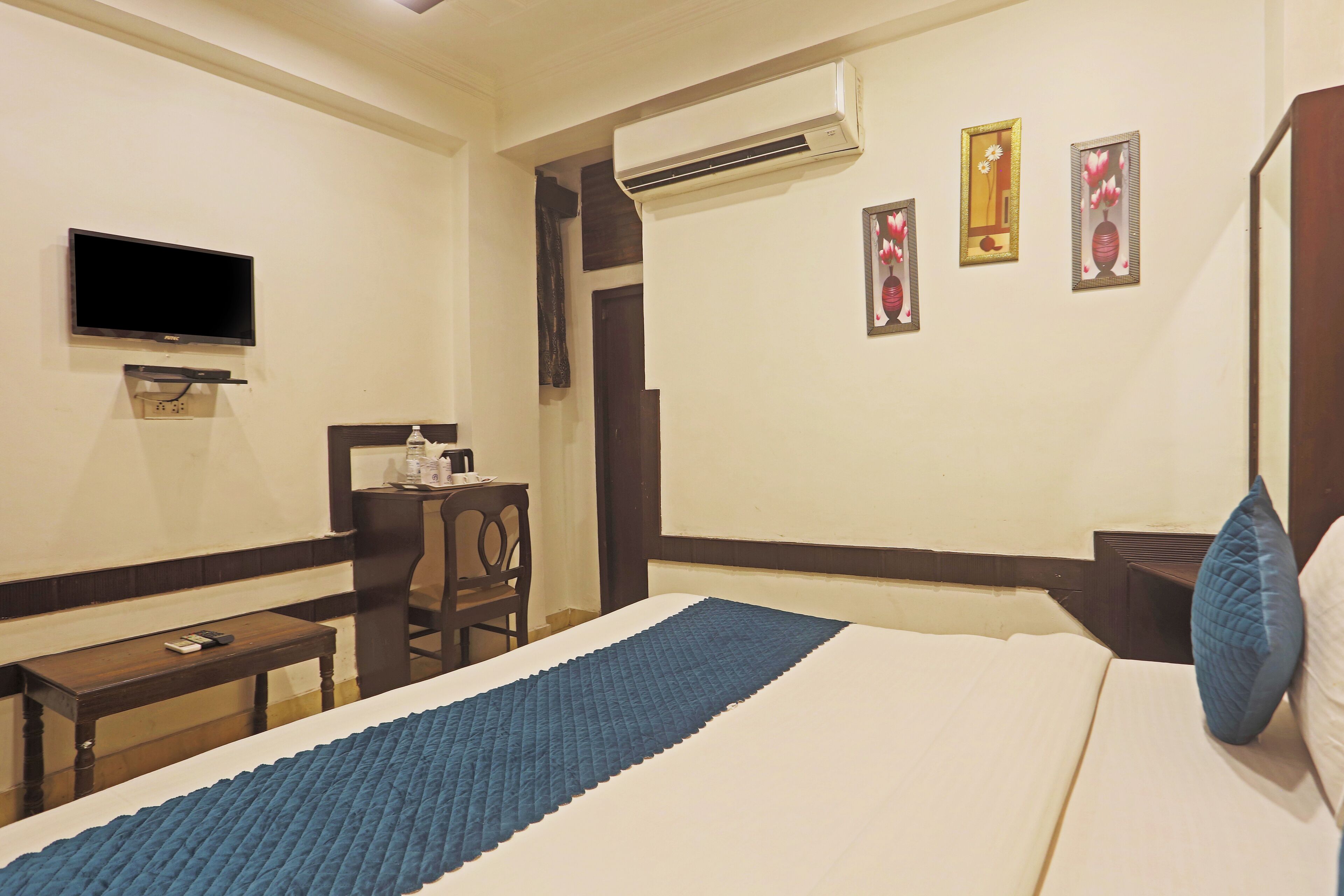 A hotel room with a bed, a desk, a chair, a TV, and an air conditioning unit.