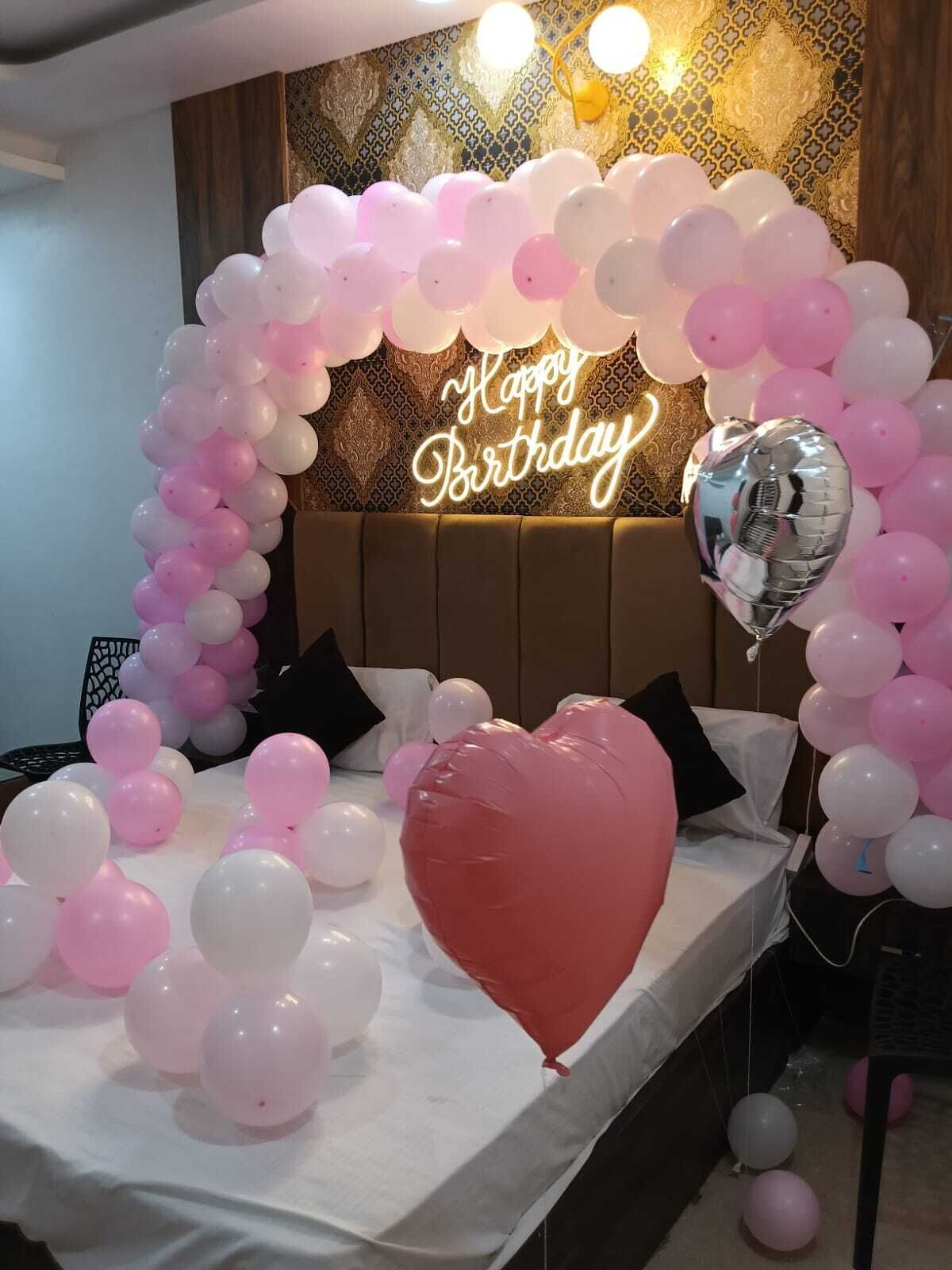 A room decorated for a birthday party with a 'Happy Birthday' sign, balloons, and a heart-shaped balloon.
