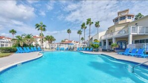 A swimming pool with blue lounge chairs, palm trees, and a building with balconies. - Whitecap Summer Resort Boat Parking Pool Hot Tub Gym (Corpus Christi)