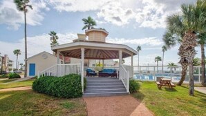 A covered outdoor area with steps leading up to a seating area, surrounded by palm trees and a view of the ocean. - Whitecap Summer Resort Boat Parking Pool Hot Tub Gym (Corpus Christi)