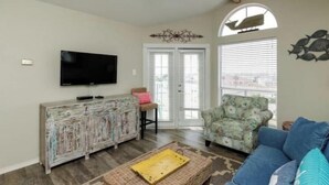 A living room with a television, a patterned armchair, a blue sofa, and a decorative wall piece. - Whitecap Summer Resort Boat Parking Pool Hot Tub Gym (Corpus Christi)