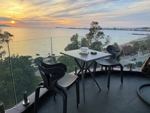 Une table et des chaises sur un balcon donnant sur une étendue d’eau, avec un coucher de soleil en arrière-plan.