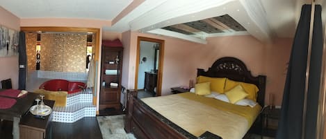 Ein Schlafzimmer mit einem großen Bett, einer Holzkommode, einem roten Sessel, einem kleinen Tisch mit einer Wasserpfeife und einem durch eine offene Tür einsehbaren Badezimmer.
