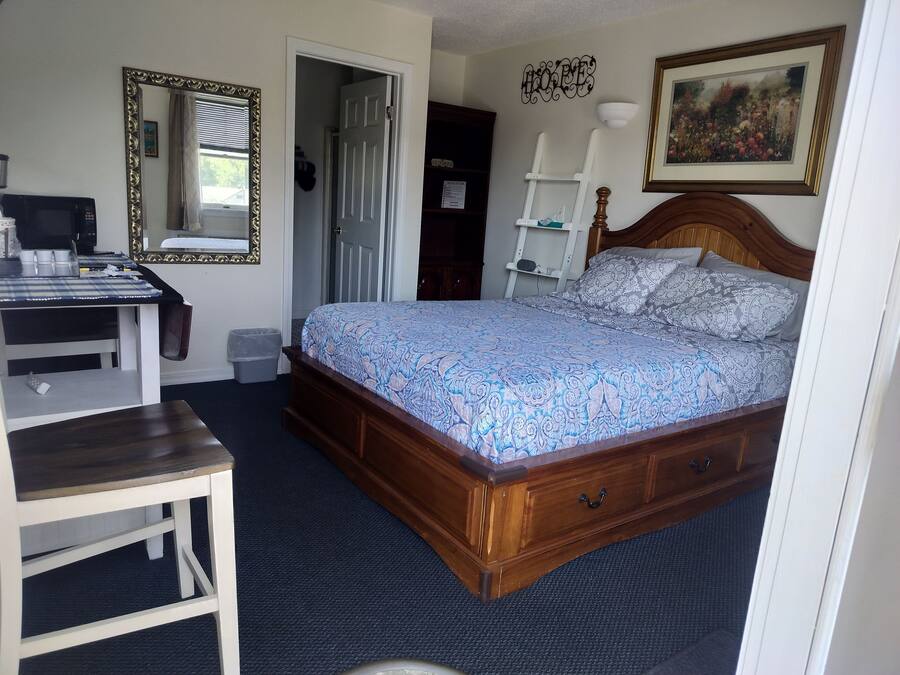 Een slaapkamer met een houten bed, een bureau, een stoel, een spiegel en een deur naar een andere kamer.