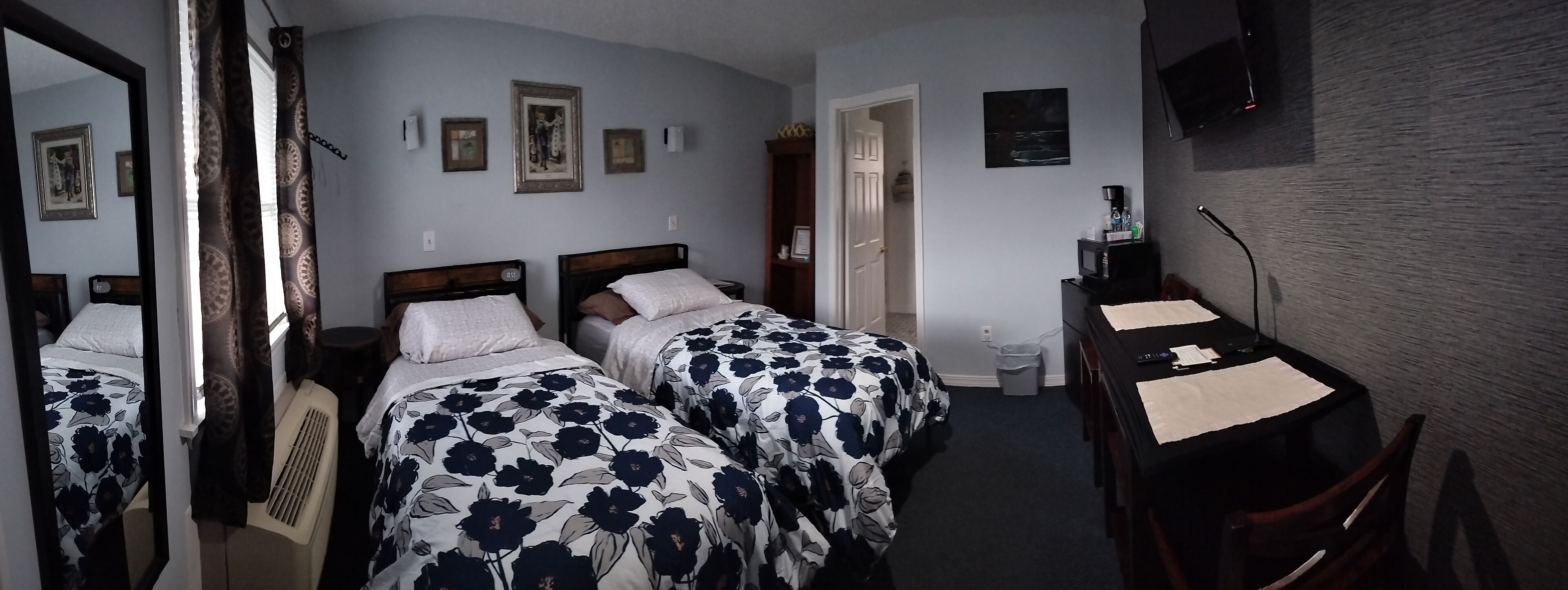 Une chambre d’hôtel avec deux lits, un bureau, une chaise, une télévision et une porte donnant sur une autre pièce.