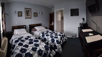 Une chambre d’hôtel avec deux lits, un bureau, une chaise, une télévision et une porte donnant sur une autre pièce.