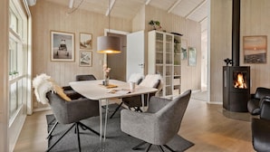 A modern living room with a white table, grey chairs, a fireplace, and wooden walls.