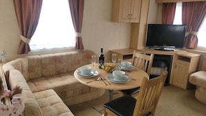 A cozy living room with a sofa, a dining table set with plates, glasses, and a bottle, and a TV on a stand.