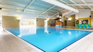 An indoor swimming pool with clear blue water, a tiled floor, and a high ceiling with visible ductwork.