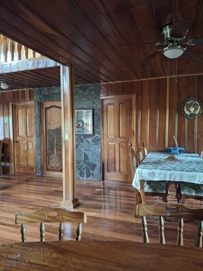 A spacious room with wooden floors, a dining table with chairs, a ceiling fan, and stone walls. - Unique, spacious, and comfortable Chalet in ideal Monteverde location. (Monteverde)