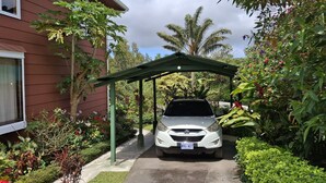 A car parked under a green canopy in front of a house with a garden. - Unique, spacious, and comfortable Chalet in ideal Monteverde location. (Monteverde)