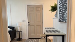 A modern kitchen with a wooden table and stools, a door, a small side table with a lamp, and a plant on the wall. - NEW Charming 2 bdrm King and Queen (North Charleston)