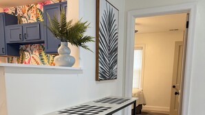 A modern kitchen with a wooden table and two stools, a potted plant, and a colorful floral wallpaper. - NEW Charming 2 bdrm King and Queen (North Charleston)