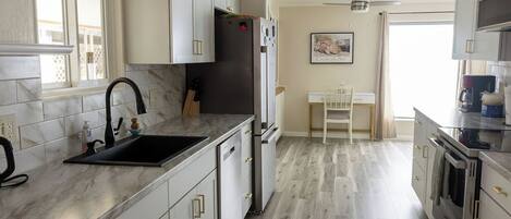 A modern kitchen with white cabinets, a black sink, and stainless steel appliances.