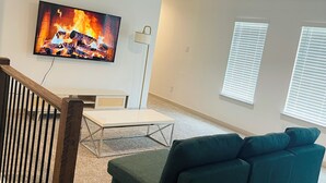 Ein Wohnzimmer mit Fernseher, Sofa, Couchtisch und einer Treppe.