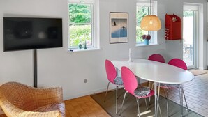 A dining area with a white table, pink chairs, a wicker chair, a TV on the wall, and a framed picture. - Lovely home in Tranekær with WiFi (Tranekær)