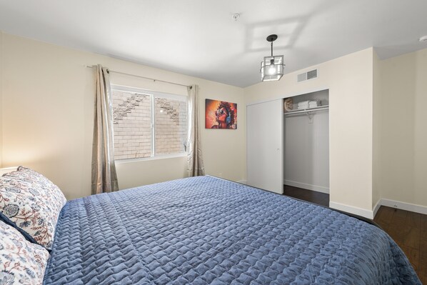 A bedroom with a large bed, a wardrobe, a window with curtains, and a painting on the wall.