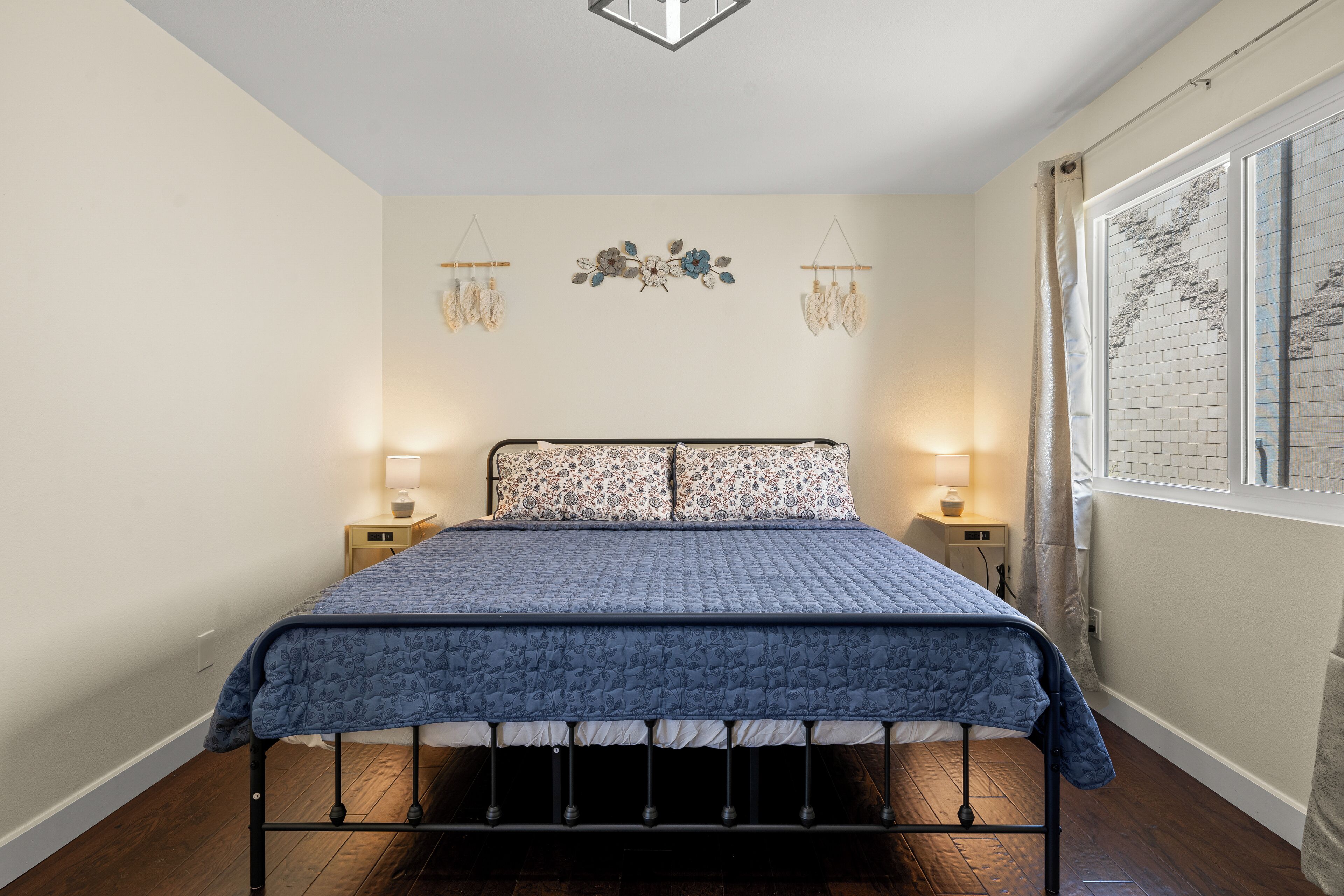 A bedroom with a bed, two bedside tables, a wall-mounted decoration, and a window with curtains.
