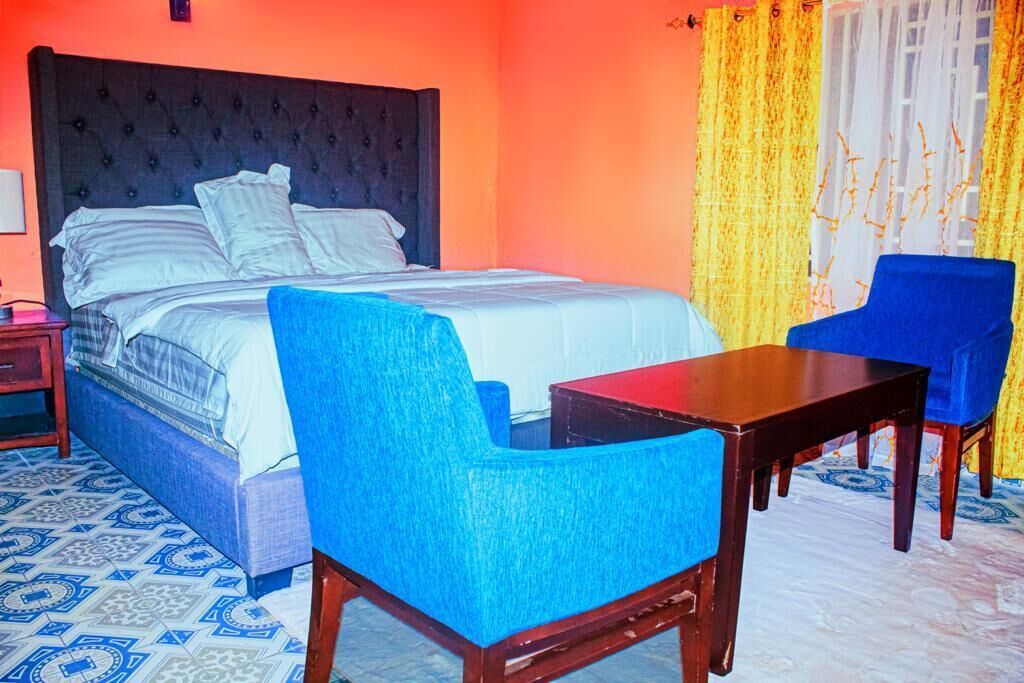 Een slaapkamer met een groot bed, een blauwe stoel, een houten tafel en een vloer met een patroon.