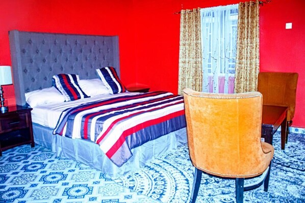 Un dormitorio con cama de cabecera capitonada, ropa de cama a rayas, suelo con diseño azul y blanco y una silla marrón.