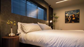 Una camera da letto moderna con un letto grande, un comodino con un vaso di fiori, un quadro appeso al muro e una finestra con persiane.