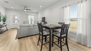 Una sala de estar moderna con un sofá gris, una mesa de comedor con sillas y un ventilador de techo.