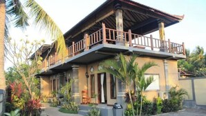 A two-story house with a balcony, surrounded by tropical plants and a small pool.