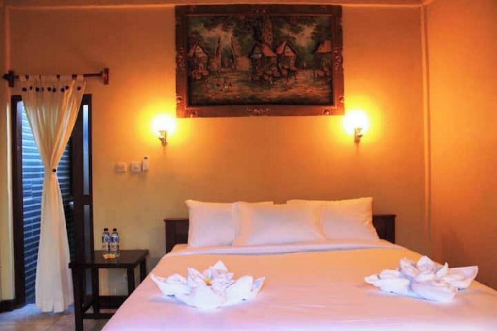 Ein Hotelzimmer mit einem Bett, zwei Wandleuchten, einem Gemälde über dem Bett und einem Nachttisch mit zwei Flaschen.
