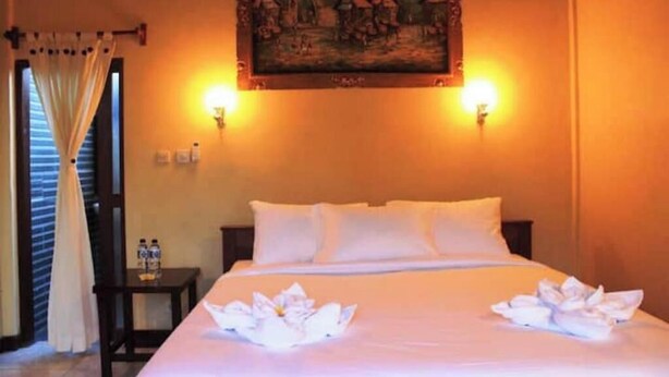 Una habitación de hotel con una cama, dos lámparas de pared, un cuadro sobre la cama y una mesita de noche con dos botellas.