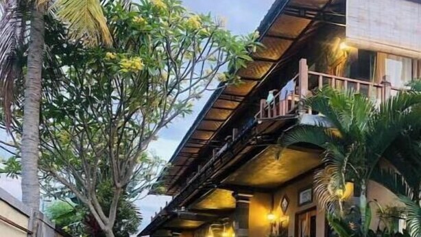 A pool area with a wooden deck, surrounded by tropical plants and a building with a balcony.
