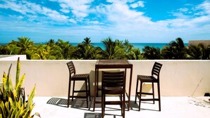 A terrace with a table and chairs, overlooking a beach with palm trees and the ocean. - Welcome to this 1 bed 1 bath condo with splendid pool view (Progreso)