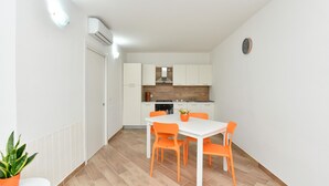A compact kitchen with white cabinets, a stove, and a sink. There is a dining table with four orange chairs and a potted plant on the floor. - Stunning home in Giungano (Giungano)