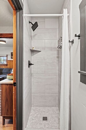 A narrow shower area with a showerhead, a shelf with toiletries, and a drain on the floor. - Timber Lodge Cabin 1 (Colorado Springs)
