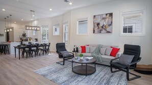 A spacious living room with a modern sofa, two armchairs, a coffee table, and a dining area with a kitchen in the background.