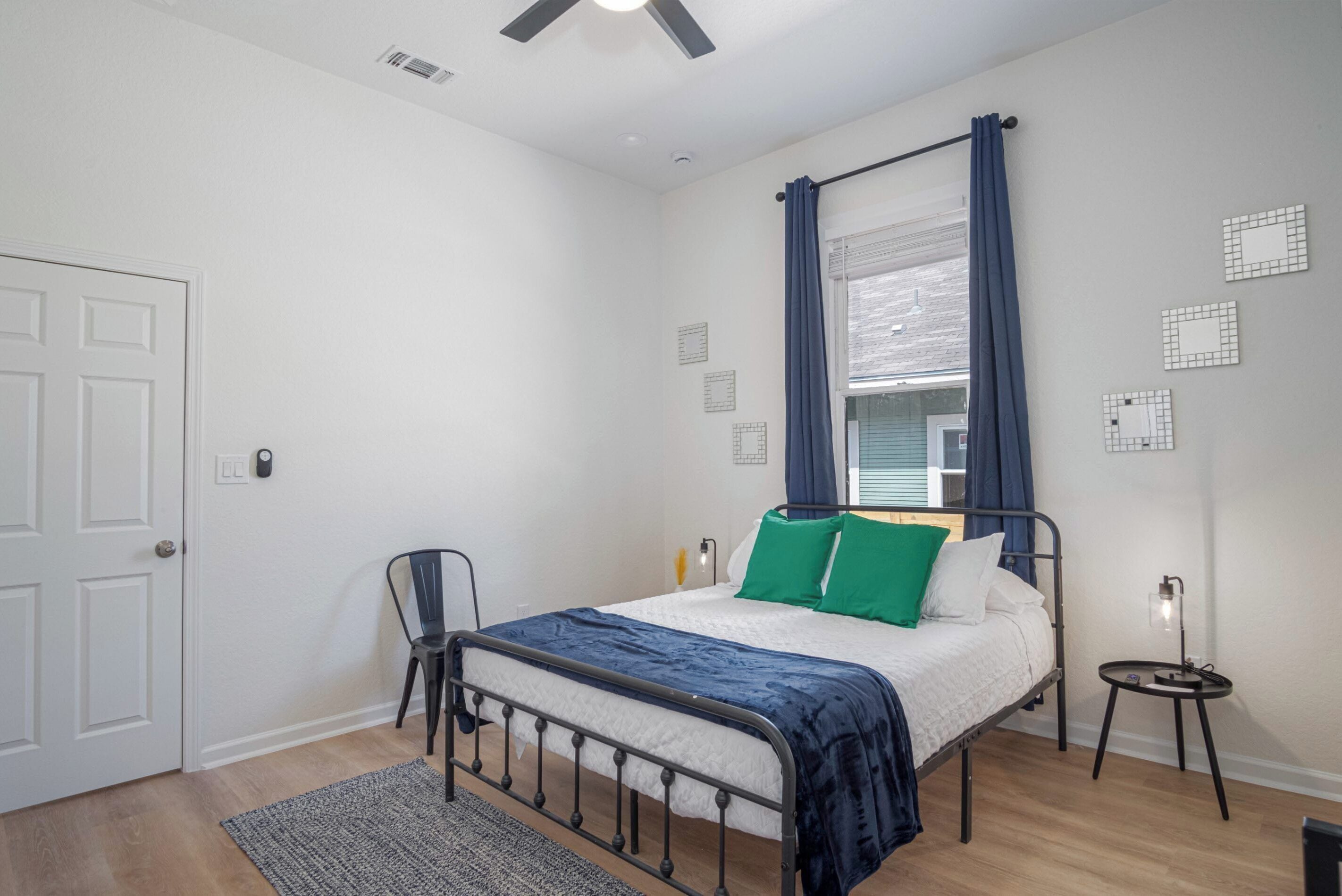 Un dormitorio con cama, una silla, una mesita de noche y una ventana con cortinas.