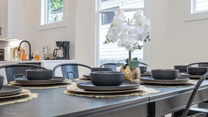 A dining table set with black bowls and plates, a vase of white orchids, and a coffee maker in the background.