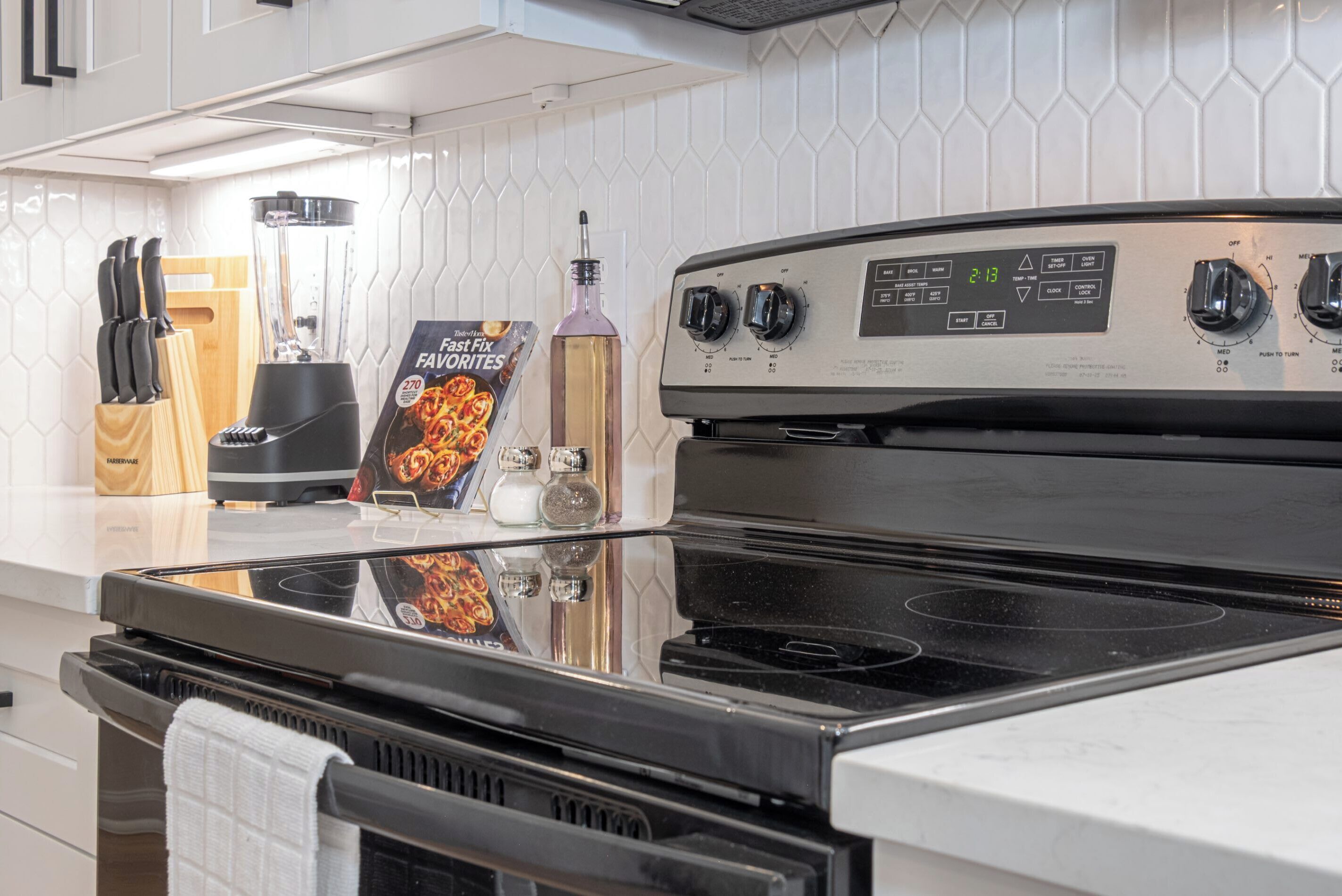 A kitchen with a black stove, a blender, a knife block, and a bottle of olive oil on the counter.
