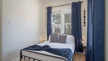 A bedroom with a bed, a bedside table, and a window with curtains.