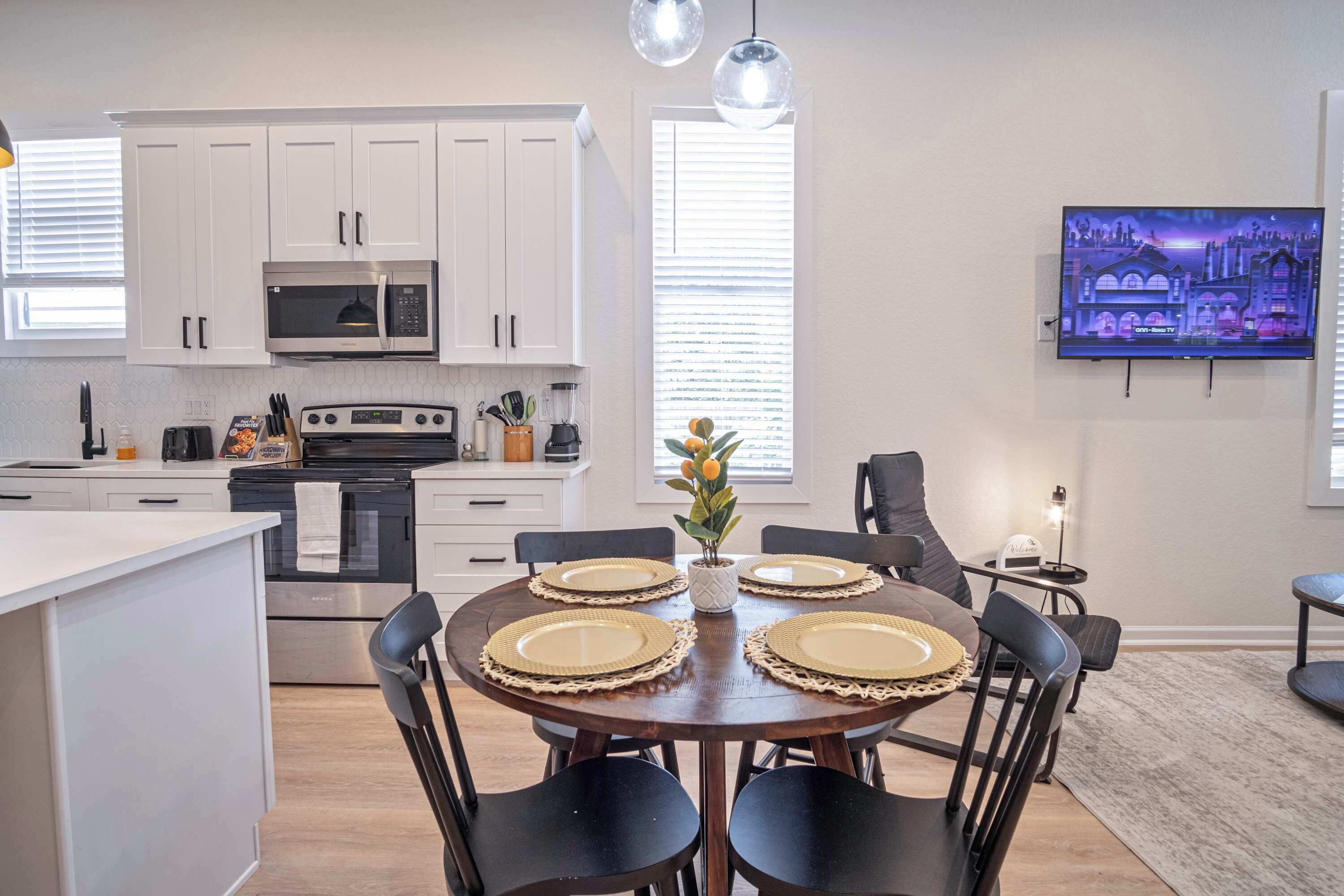 A modern kitchen with white cabinets, a microwave, and a dining area with a round table set for four.