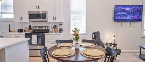 A modern kitchen with white cabinets, a microwave, and a dining area with a round table set for four.