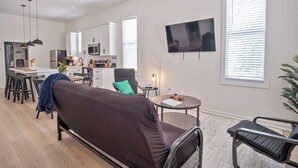 A modern living room with a sofa, a dining area with chairs, a kitchen with cabinets and appliances, and a TV mounted on the wall. - Walk to Riverwalk! 3br/2ba Gem Near Fun Downtown! (San Antonio)