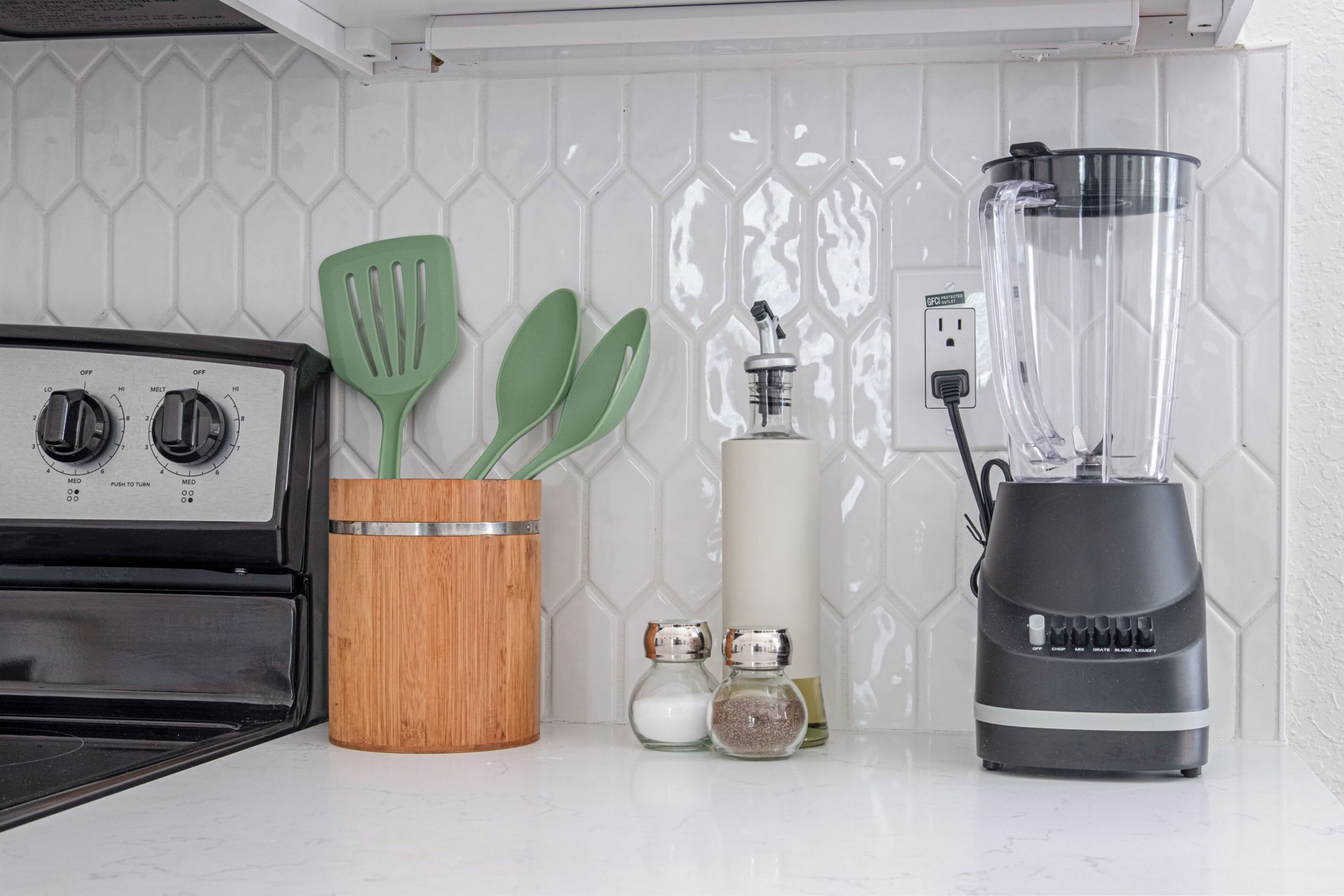 A kitchen with a stove, a blender, and a wooden utensil holder.