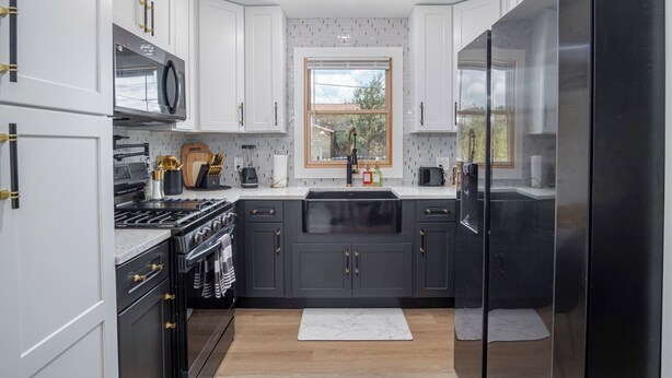 A modern kitchen with white and dark grey cabinets, a black refrigerator, and a window above the sink. - Stylish Stay With Unforgettable Downtown Views! (San Antonio)
