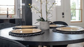 A round dining table with a dark wood finish, surrounded by chairs. A woven centerpiece with white flowers is placed in the middle. - Stylish Stay With Unforgettable Downtown Views! (San Antonio)