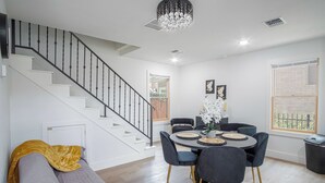 A modern living room with a staircase, a dining area with a round table and chairs, and a large window with a view. - Stylish Stay With Unforgettable Downtown Views! (San Antonio)