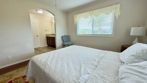 Quarto com cama, cadeira, janela com persianas, mesa de cabeceira e abajur.